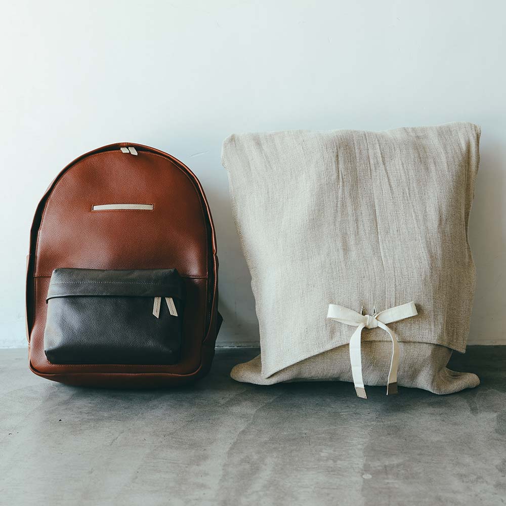 ラウンドレザーバックパック - ギフトラッピング選択で、ジュート素材（※）のオリジナルバッグに包んでお届けします。（※ジュートは燃やしても有害物質が出ず、土に還るサスティナブルな自然素材。原料も育ちが早く、二酸化炭素の吸収力が高く、地球温暖化を抑制する働きもあります）